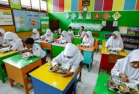 Inovasi Skema MBG Ramadan: Menu Bawa Pulang untuk Anak Sekolah

Pemerintah meluncurkan pendekatan baru dalam program Makan Bergizi Gratis (MBG) bagi anak sekolah selama bulan Ramadan. Dalam skema yang diperbarui, makanan tidak hanya dikonsumsi di sekolah, tetapi juga disediakan untuk dibawa pulang, sehingga dapat dinikmati saat berbuka puasa.

Kepala Badan Gizi Nasional, Dadan Hindayana, menjelaskan bahwa mekanisme baru ini sudah diberlakukan sejak 6 Maret 2025. “Meski konsepnya berubah, besaran biaya MBG selama Ramadan tetap sama seperti hari biasa. Semua anak sekolah akan menerima makanan yang bisa dibawa pulang secara serempak,” ungkapnya.

Detail Skema dan Menu
Menurut Dadan, menu MBG dirancang agar tahan lama, sehingga aman untuk disimpan hingga waktu berbuka puasa. Menu tersebut meliputi telur rebus, susu, kurma, kue kering fortifikasi, dan buah-buahan. “Kami juga menambahkan variasi seperti bubur kacang hijau atau kolak secara berkala, untuk memastikan komposisi gizinya tetap seimbang antara protein, karbohidrat, dan serat,” tambahnya.

Sebelumnya, pelaksanaan MBG dilakukan pada pagi hari sekitar pukul 09.00 WIB, yang membuat jarak waktu cukup jauh hingga saat berbuka puasa sekitar pukul 18.00 WIB. Dengan skema baru ini, anak-anak bisa menikmati makanan bergizi tepat waktu sesuai kebutuhan puasa.

Mekanisme Baru Pelaksanaan
Dalam penjelasan di Istana Negara, Dadan menyampaikan bahwa perubahan ini bertujuan untuk mengakomodasi kebutuhan anak yang berpuasa. “Walaupun sekolah tetap beroperasi dan program MBG dilaksanakan, mekanismenya diubah. Makanan yang disediakan bisa langsung dibawa pulang sehingga dapat dinikmati saat buka puasa bagi yang menjalankan ibadah, sementara bagi yang tidak berpuasa, bisa dikonsumsi di sekolah atau di rumah,” jelasnya.

Pihak pemerintah juga menegaskan bahwa meski terdapat inovasi dalam penyaluran, kualitas makanan tetap menjadi prioritas utama. Akreditasi terhadap Satuan Pelayanan Pemenuhan Gizi (SPPG) akan dilakukan oleh lembaga independen, yang akan memberikan penilaian mulai dari kategori unggul, baik sekali, hingga baik, jika jumlah SPPG sudah mencapai 2.000 unit. Proses intervensi ini akan berjalan hingga Agustus 2025.

Tanggapan dari Berbagai Pihak
Sebelumnya, beberapa laporan menyebutkan bahwa standar MBG di berbagai daerah belum konsisten. Masalah mulai dari makanan yang tidak sesuai standar gizi hingga kejadian keracunan pada siswa sempat mencuat. Direktur Eksekutif Global Strategi Riset Indonesia (GSRI), Sebastian Salang, menegaskan pentingnya perbaikan dari hulu, yakni di bagian pengolahan di SPPG. Menurutnya, kurangnya quality control (QC) di dapur umum menyebabkan penyajian makanan tidak optimal.

“Saat ini banyak berita mengenai ketidaksesuaian pelaksanaan MBG, terutama di media sosial dan platform online. Dari riset yang kami lakukan, terlihat jelas bahwa konsep dan perencanaan awal belum matang. Hal ini berdampak pada kesiapan di lapangan ketika program dimulai pada Januari,” papar Sebastian.

Dengan penerapan skema baru ini, diharapkan program MBG dapat berjalan lebih efektif, aman, dan sesuai dengan kebutuhan anak-anak selama bulan suci Ramadan.