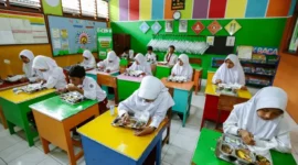 Inovasi Skema MBG Ramadan: Menu Bawa Pulang untuk Anak Sekolah

Pemerintah meluncurkan pendekatan baru dalam program Makan Bergizi Gratis (MBG) bagi anak sekolah selama bulan Ramadan. Dalam skema yang diperbarui, makanan tidak hanya dikonsumsi di sekolah, tetapi juga disediakan untuk dibawa pulang, sehingga dapat dinikmati saat berbuka puasa.

Kepala Badan Gizi Nasional, Dadan Hindayana, menjelaskan bahwa mekanisme baru ini sudah diberlakukan sejak 6 Maret 2025. “Meski konsepnya berubah, besaran biaya MBG selama Ramadan tetap sama seperti hari biasa. Semua anak sekolah akan menerima makanan yang bisa dibawa pulang secara serempak,” ungkapnya.

Detail Skema dan Menu
Menurut Dadan, menu MBG dirancang agar tahan lama, sehingga aman untuk disimpan hingga waktu berbuka puasa. Menu tersebut meliputi telur rebus, susu, kurma, kue kering fortifikasi, dan buah-buahan. “Kami juga menambahkan variasi seperti bubur kacang hijau atau kolak secara berkala, untuk memastikan komposisi gizinya tetap seimbang antara protein, karbohidrat, dan serat,” tambahnya.

Sebelumnya, pelaksanaan MBG dilakukan pada pagi hari sekitar pukul 09.00 WIB, yang membuat jarak waktu cukup jauh hingga saat berbuka puasa sekitar pukul 18.00 WIB. Dengan skema baru ini, anak-anak bisa menikmati makanan bergizi tepat waktu sesuai kebutuhan puasa.

Mekanisme Baru Pelaksanaan
Dalam penjelasan di Istana Negara, Dadan menyampaikan bahwa perubahan ini bertujuan untuk mengakomodasi kebutuhan anak yang berpuasa. “Walaupun sekolah tetap beroperasi dan program MBG dilaksanakan, mekanismenya diubah. Makanan yang disediakan bisa langsung dibawa pulang sehingga dapat dinikmati saat buka puasa bagi yang menjalankan ibadah, sementara bagi yang tidak berpuasa, bisa dikonsumsi di sekolah atau di rumah,” jelasnya.

Pihak pemerintah juga menegaskan bahwa meski terdapat inovasi dalam penyaluran, kualitas makanan tetap menjadi prioritas utama. Akreditasi terhadap Satuan Pelayanan Pemenuhan Gizi (SPPG) akan dilakukan oleh lembaga independen, yang akan memberikan penilaian mulai dari kategori unggul, baik sekali, hingga baik, jika jumlah SPPG sudah mencapai 2.000 unit. Proses intervensi ini akan berjalan hingga Agustus 2025.

Tanggapan dari Berbagai Pihak
Sebelumnya, beberapa laporan menyebutkan bahwa standar MBG di berbagai daerah belum konsisten. Masalah mulai dari makanan yang tidak sesuai standar gizi hingga kejadian keracunan pada siswa sempat mencuat. Direktur Eksekutif Global Strategi Riset Indonesia (GSRI), Sebastian Salang, menegaskan pentingnya perbaikan dari hulu, yakni di bagian pengolahan di SPPG. Menurutnya, kurangnya quality control (QC) di dapur umum menyebabkan penyajian makanan tidak optimal.

“Saat ini banyak berita mengenai ketidaksesuaian pelaksanaan MBG, terutama di media sosial dan platform online. Dari riset yang kami lakukan, terlihat jelas bahwa konsep dan perencanaan awal belum matang. Hal ini berdampak pada kesiapan di lapangan ketika program dimulai pada Januari,” papar Sebastian.

Dengan penerapan skema baru ini, diharapkan program MBG dapat berjalan lebih efektif, aman, dan sesuai dengan kebutuhan anak-anak selama bulan suci Ramadan.